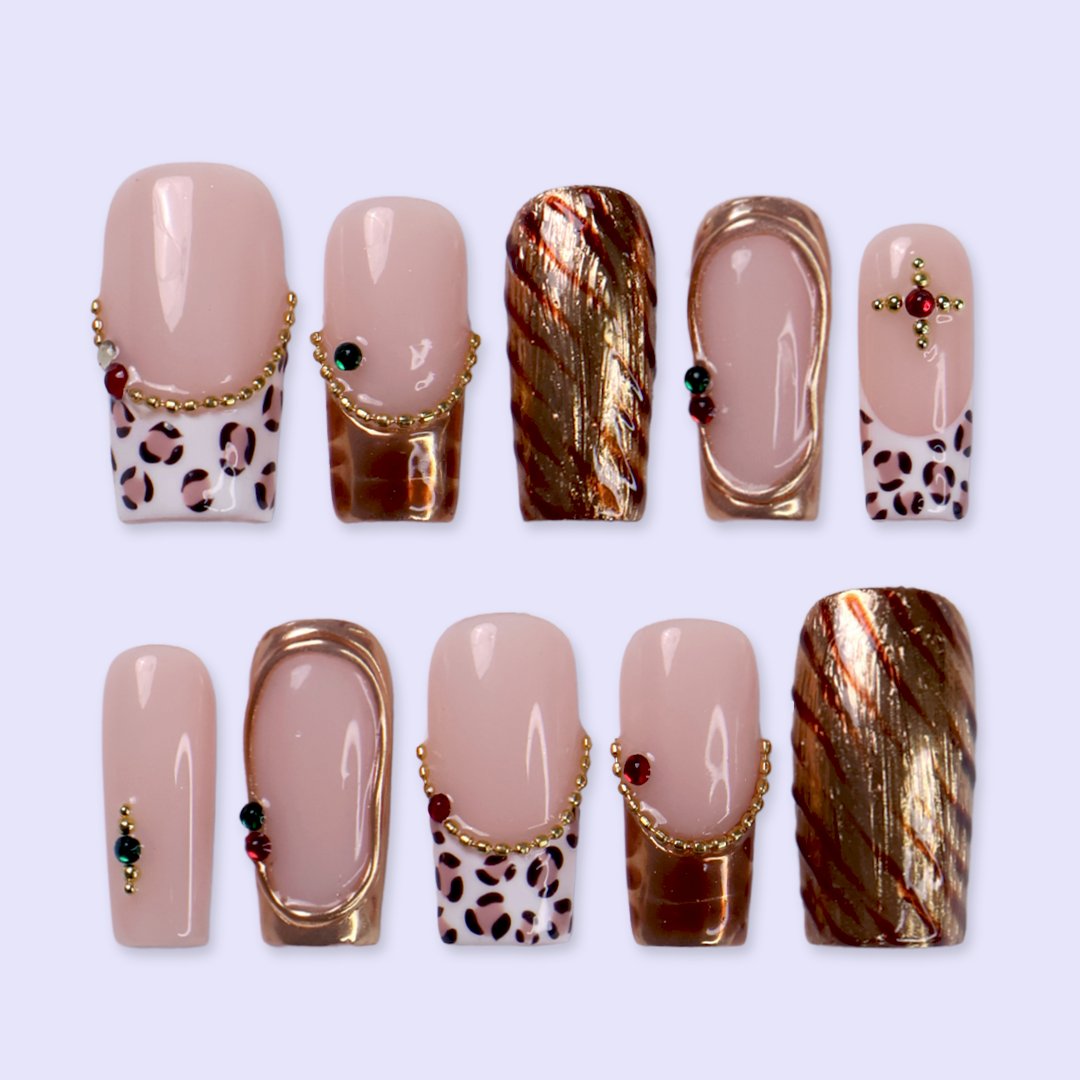 Moscato handmade fall press-on nails — medium square set in nude with leopard-print French tips, metallic gold tiger-stripe foil, gold mirror frame and red and green gemstone accents.