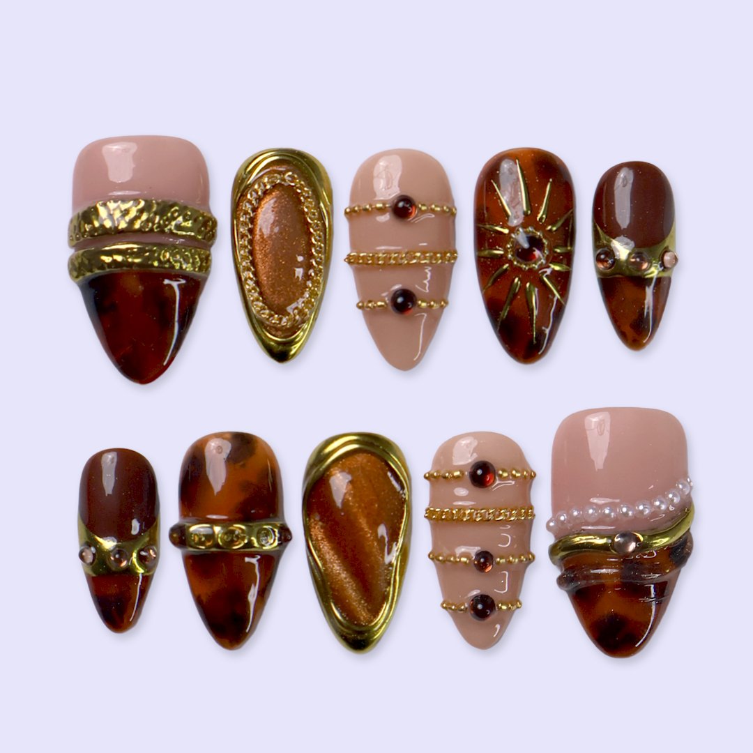 Jasper handmade fall press-on nails — maximalist almond set in nude and tortoiseshell brown with gold cat-eye cabochons, ornate gold frames, sunburst, delicate chains, amber gemstones and pearl accents.