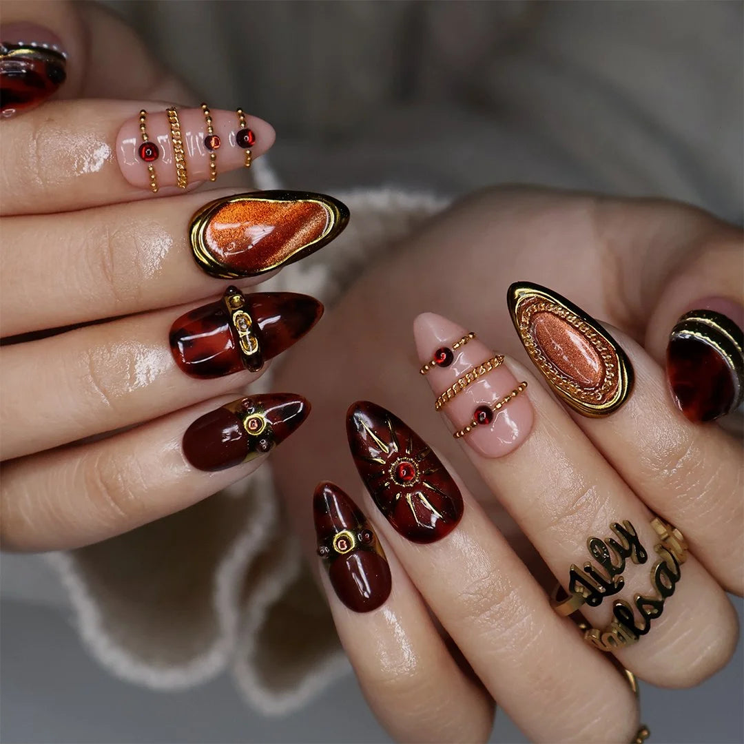 Jasper handmade fall press-on nails — maximalist almond set in nude and tortoiseshell brown with gold cat-eye cabochons, ornate gold frames, sunburst, delicate chains, amber gemstones and pearl accents.
