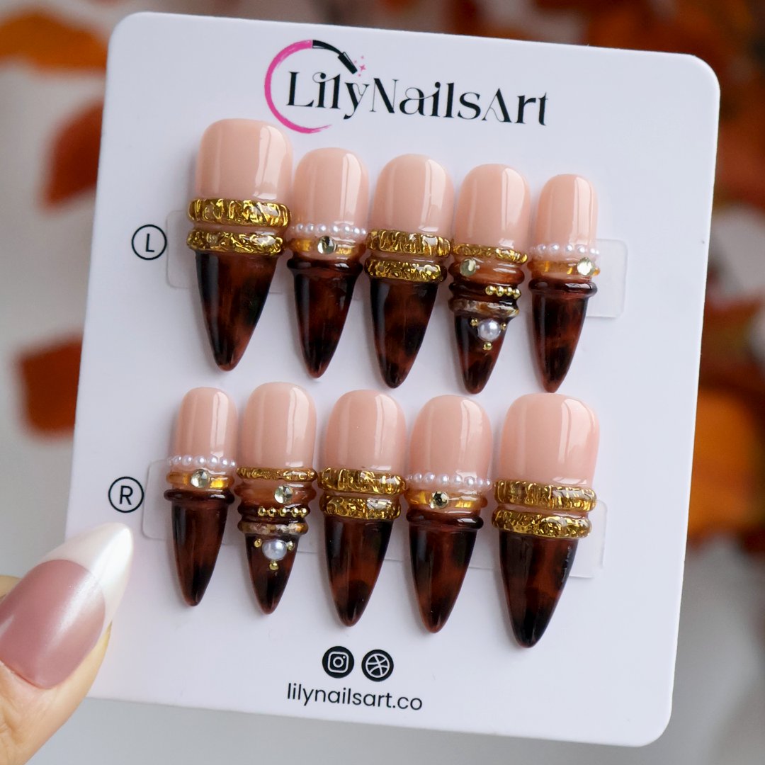 Bourbon handmade fall press-on nails — long almond set in nude fading into deep tortoiseshell brown with textured gold bands, delicate pearls and sparkling gemstone accents.