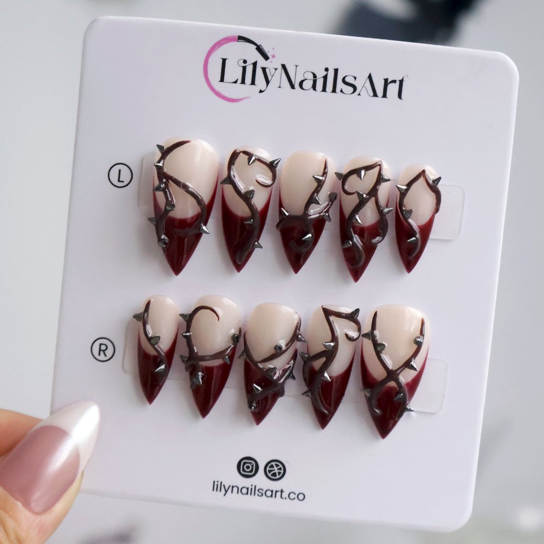 Forbidden gothic press on nails in nude and blood-red French tips with sculpted 3D thorny vines and silver spikes — handmade Halloween press on nails, long stiletto fake nails and gothic nail art.