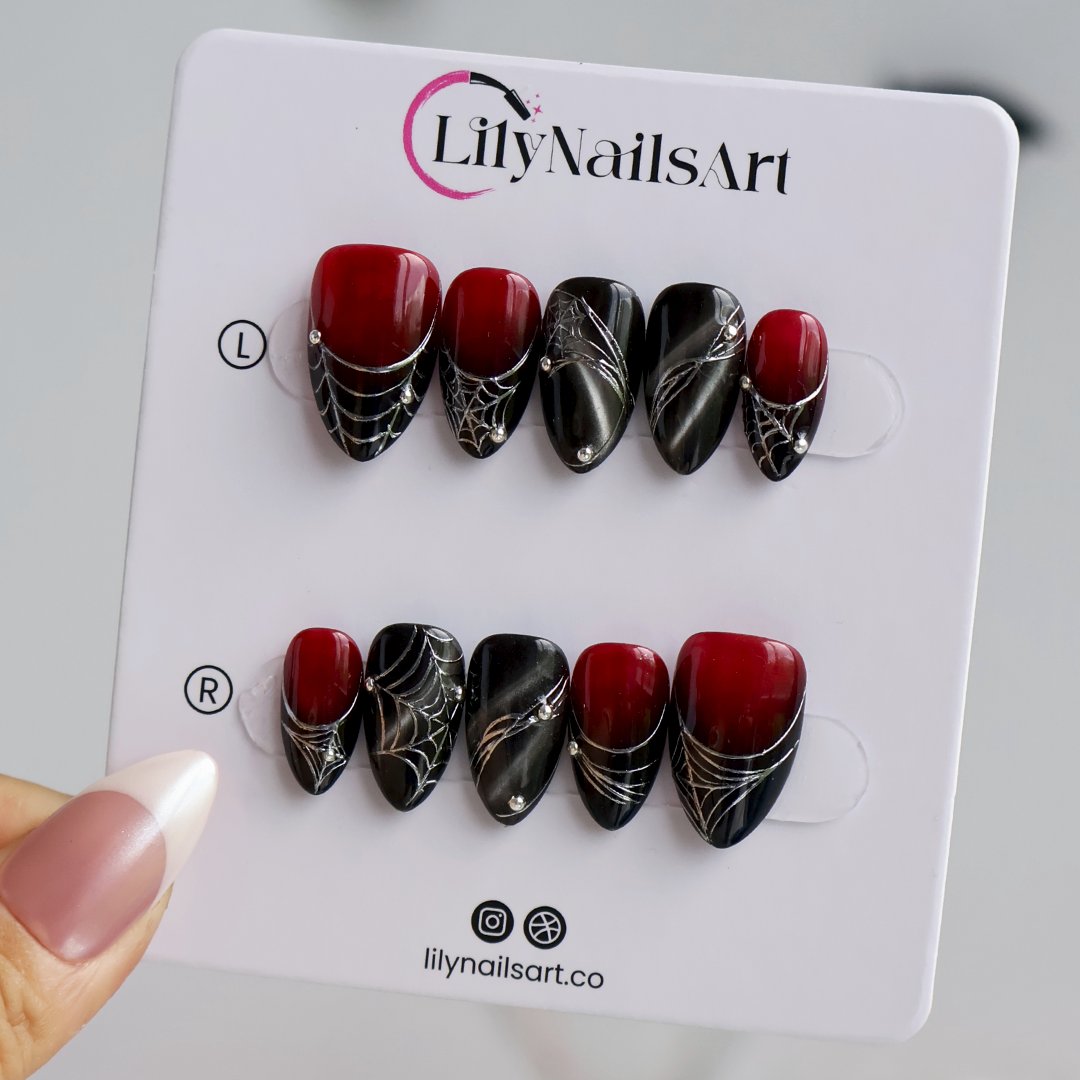 Arachne handmade gothic Halloween press-on nails — short almond set in blood-red and black cat-eye shimmer with silver spiderwebs and metallic bead accents.