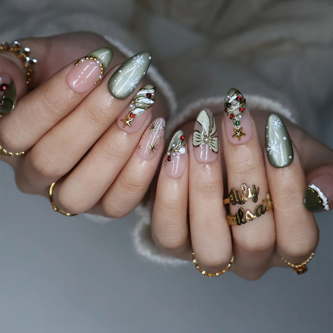 Wintergreen handmade Christmas press-on nails — medium almond set in nude and sage-green cat-eye with a 3D gold-star Christmas tree, delicate snowflakes, gold bow, ornament baubles and red-green gemstone accents.