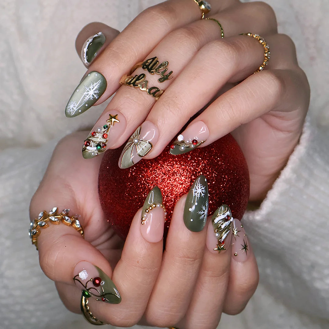 Wintergreen handmade Christmas press-on nails — medium almond set in nude and sage-green cat-eye with a 3D gold-star Christmas tree, delicate snowflakes, gold bow, ornament baubles and red-green gemstone accents.