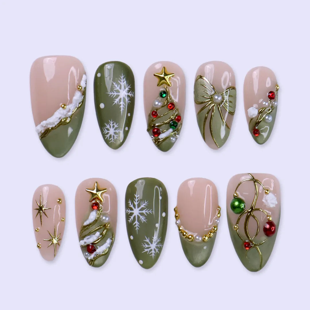 Wintergreen handmade Christmas press-on nails — medium almond set in nude and sage-green cat-eye with a 3D gold-star Christmas tree, delicate snowflakes, gold bow, ornament baubles and red-green gemstone accents.