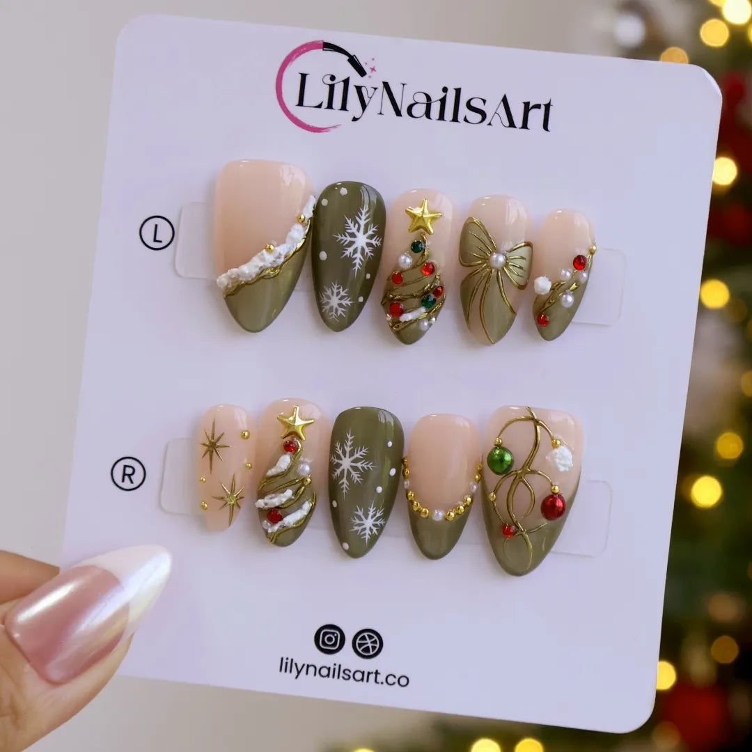 Wintergreen handmade Christmas press-on nails — medium almond set in nude and sage-green cat-eye with a 3D gold-star Christmas tree, delicate snowflakes, gold bow, ornament baubles and red-green gemstone accents.