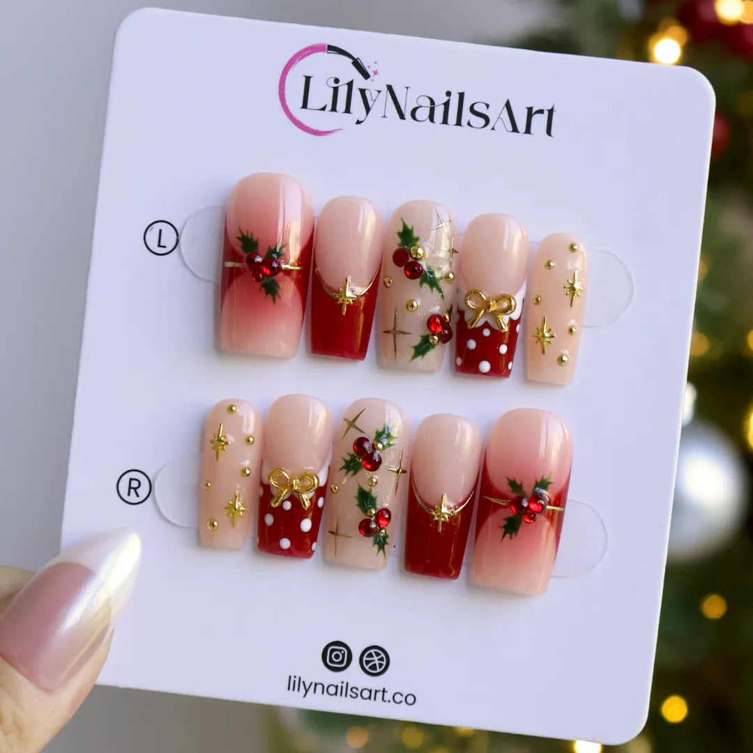 Hollytini handmade Christmas press-on nails — medium square set in nude and red with holly berries, gold bows, gold starbursts, white polka dots and sparkling red gemstone accents.