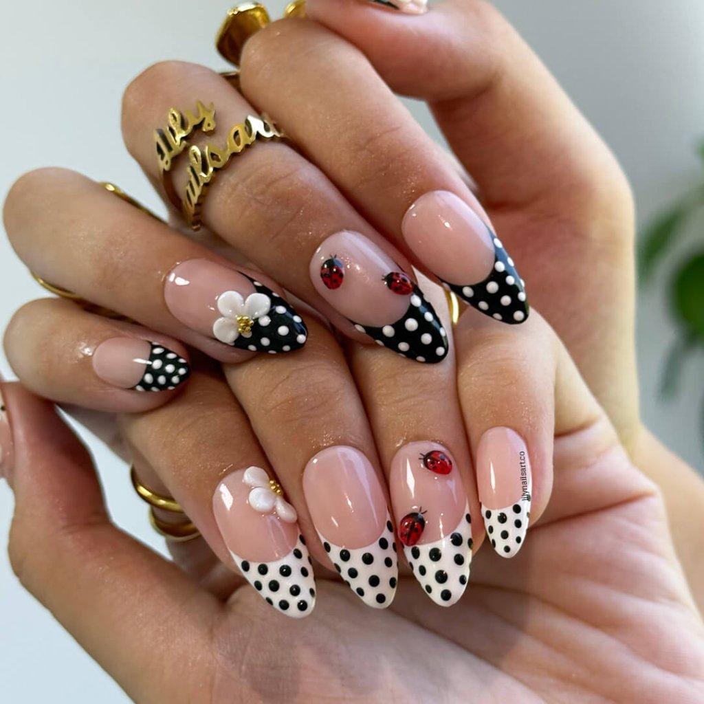 Hand with intricately designed nails featuring polka dots, flowers, and ladybugs.