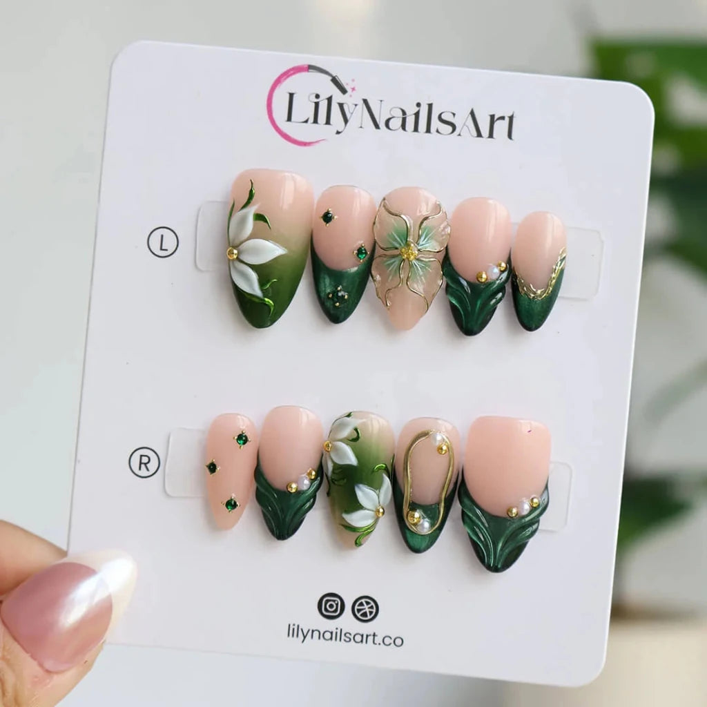 3D emerald green press on nails with white lily florals and gold vine accents, embellished with emerald crystals, pearls, and gold chain details on a nude base — custom press on nails, luxury handmade nail art, fake nails, false nails, pressons — perfect for prom, galas, and emerald-themed events