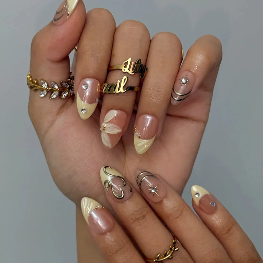 3D gold chrome French tip press on nails with swirl accents, embellished with starburst crystals and white floral details on a nude base — custom press on nails, luxury handmade nail art, fake nails, false nails, pressons — perfect for prom, weddings, and spring events