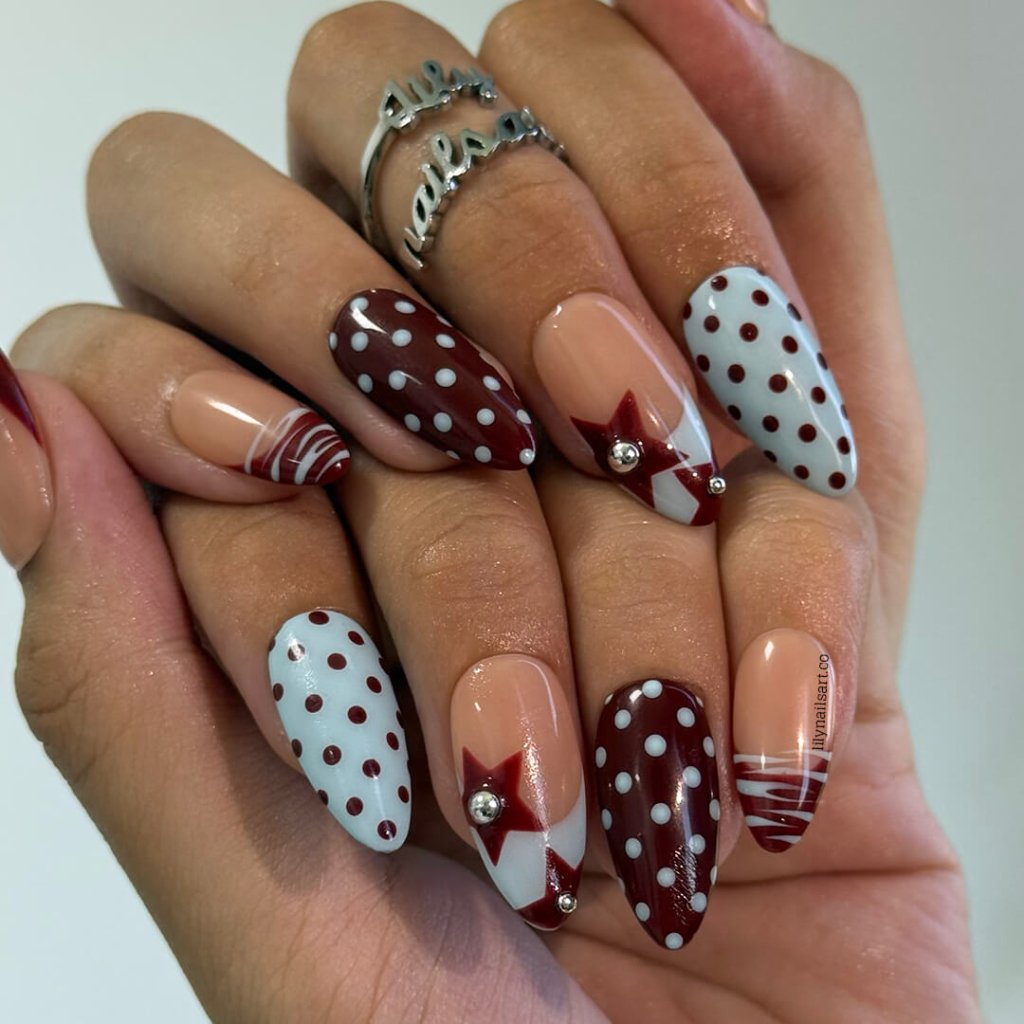 Handmade almond press on nails featuring a playful mix of burgundy polka dots, nude base with burgundy geometric tips, silver bead accents, and abstract line art. Retro-inspired, perfect for a bold and stylish look.