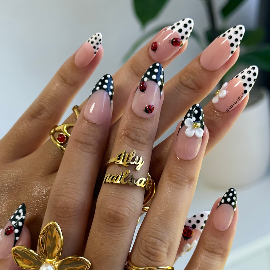 Nails with polka dot and floral designs, wearing gold rings, on a neutral background.