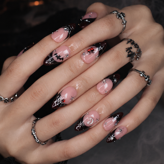 Samhain handmade gothic Halloween press-on nails — medium almond set in nude with black French tips, silver starbursts, bat, jeweled spider, spiderwebs and crescent moon.