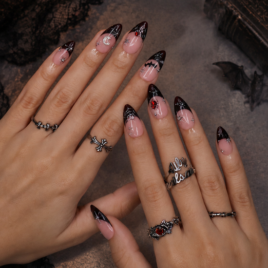 Samhain handmade gothic Halloween press-on nails — medium almond set in nude with black French tips, silver starbursts, bat, jeweled spider, spiderwebs and crescent moon.