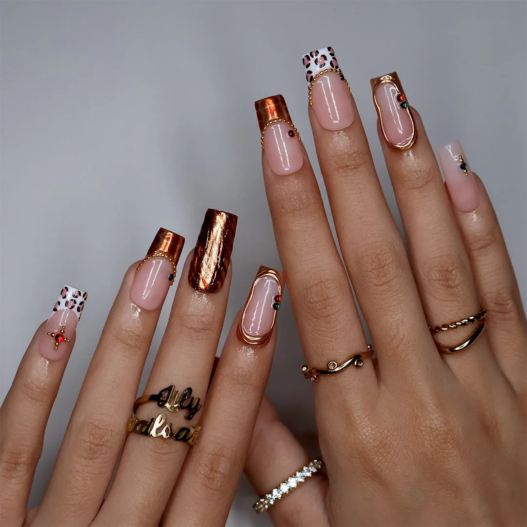 Moscato handmade fall press-on nails — medium square set in nude with leopard-print French tips, metallic gold tiger-stripe foil, gold mirror frame and red and green gemstone accents.