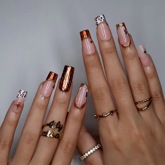 Moscato handmade fall press-on nails — medium square set in nude with leopard-print French tips, metallic gold tiger-stripe foil, gold mirror frame and red and green gemstone accents.