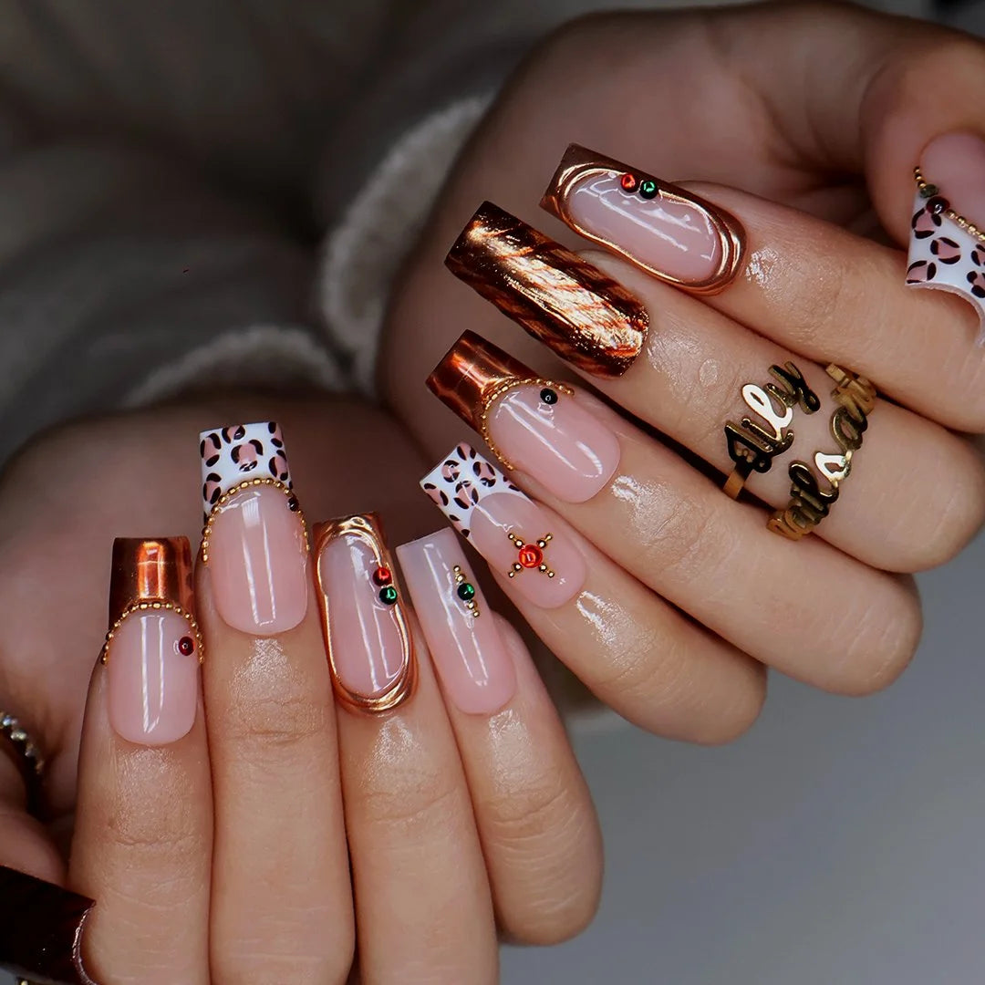 Moscato handmade fall press-on nails — medium square set in nude with leopard-print French tips, metallic gold tiger-stripe foil, gold mirror frame and red and green gemstone accents.