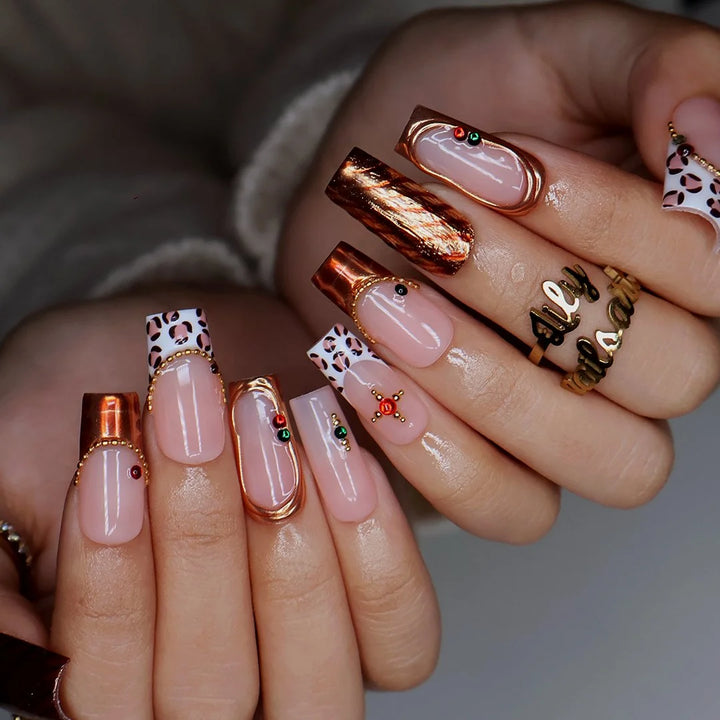 Moscato handmade fall press-on nails — medium square set in nude with leopard-print French tips, metallic gold tiger-stripe foil, gold mirror frame and red and green gemstone accents.