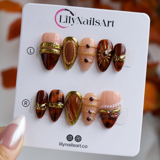 Jasper handmade fall press-on nails — maximalist almond set in nude and tortoiseshell brown with gold cat-eye cabochons, ornate gold frames, sunburst, delicate chains, amber gemstones and pearl accents.