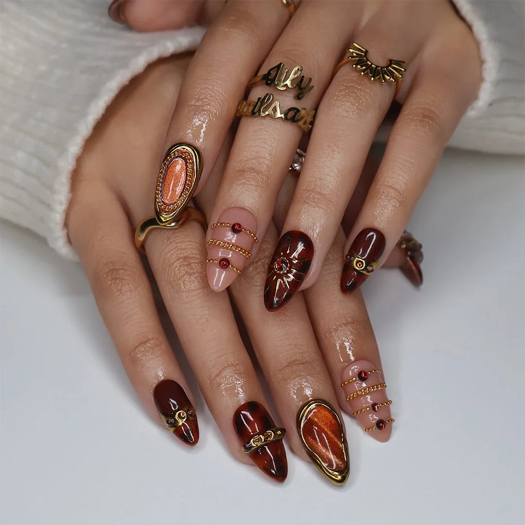Jasper handmade fall press-on nails — maximalist almond set in nude and tortoiseshell brown with gold cat-eye cabochons, ornate gold frames, sunburst, delicate chains, amber gemstones and pearl accents.