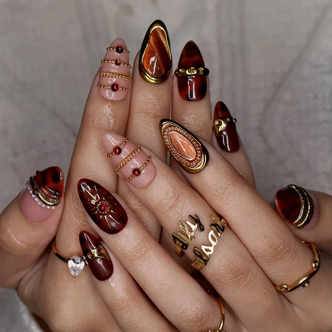 Jasper handmade fall press-on nails — maximalist almond set in nude and tortoiseshell brown with gold cat-eye cabochons, ornate gold frames, sunburst, delicate chains, amber gemstones and pearl accents.