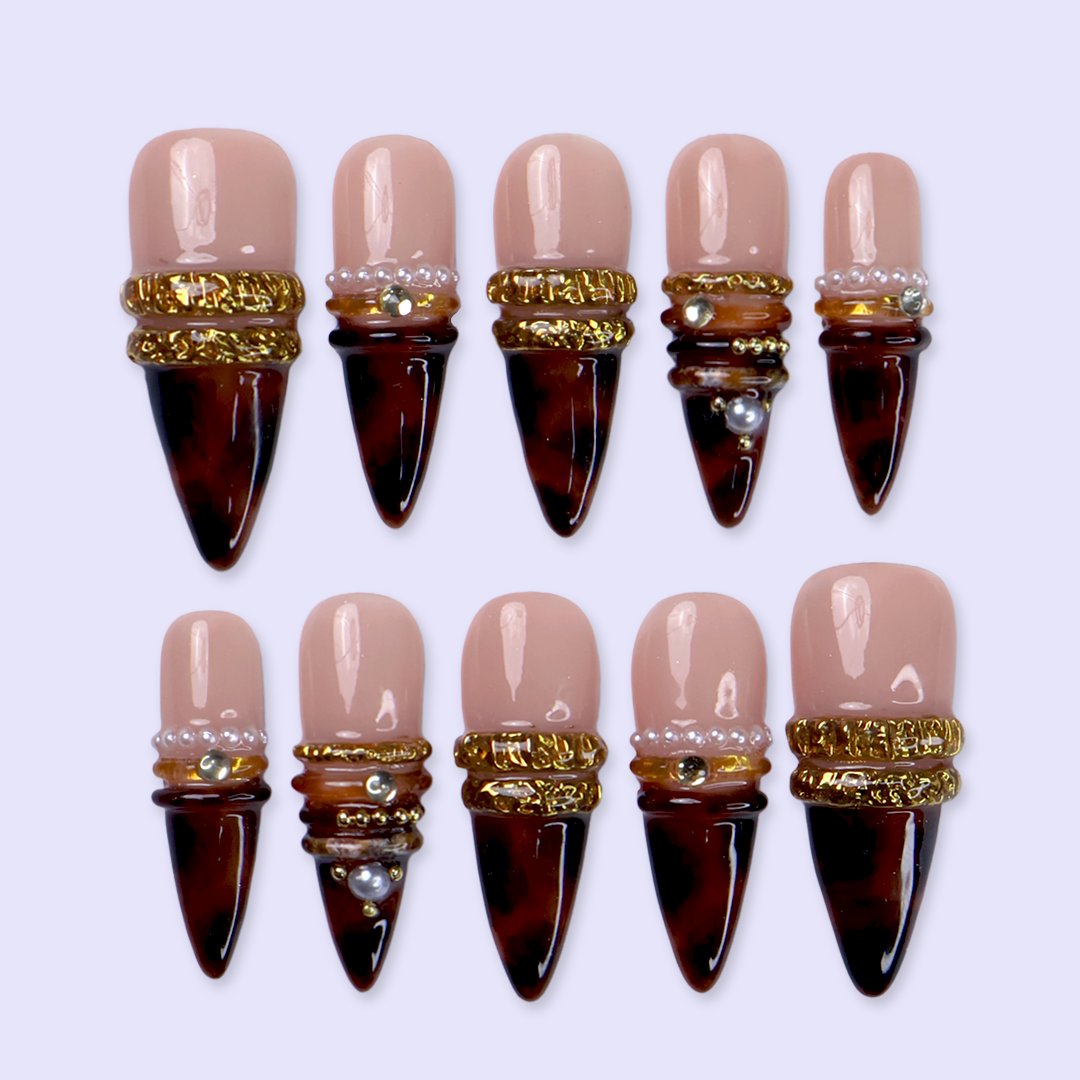 Bourbon handmade fall press-on nails — long almond set in nude fading into deep tortoiseshell brown with textured gold bands, delicate pearls and sparkling gemstone accents.