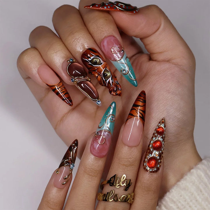 Tigress handmade fall press-on nails — maximalist long almond set with hand-painted 3D tiger faces, piercing green eyes, tiger stripes, gold-framed cat-eye cabochons, sculpted gold swirls and turquoise accents.