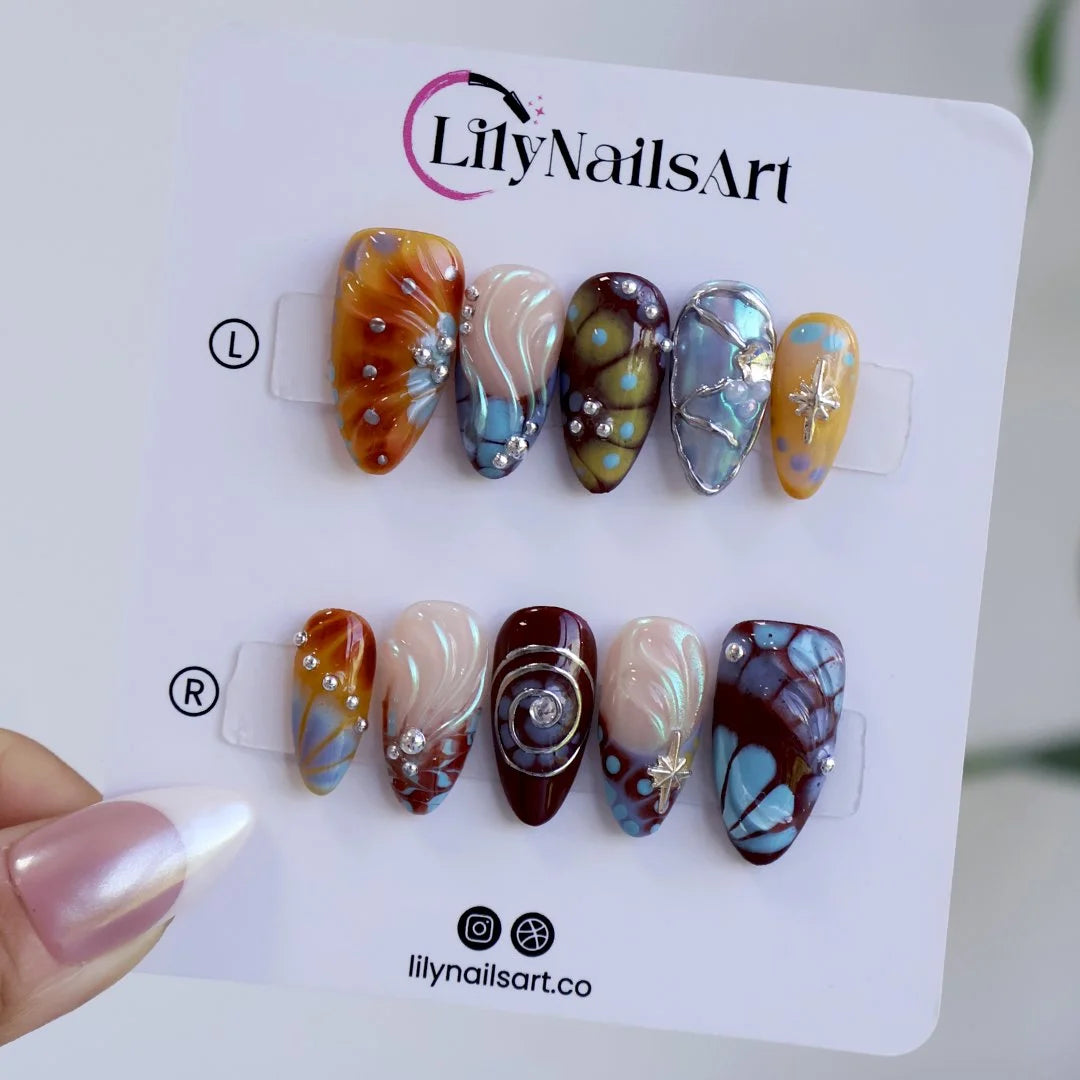 Asteria handmade Y2K press-on nails — almond set in caramel, brown and sky blue with silver chrome swirls, starbursts and marble effects
