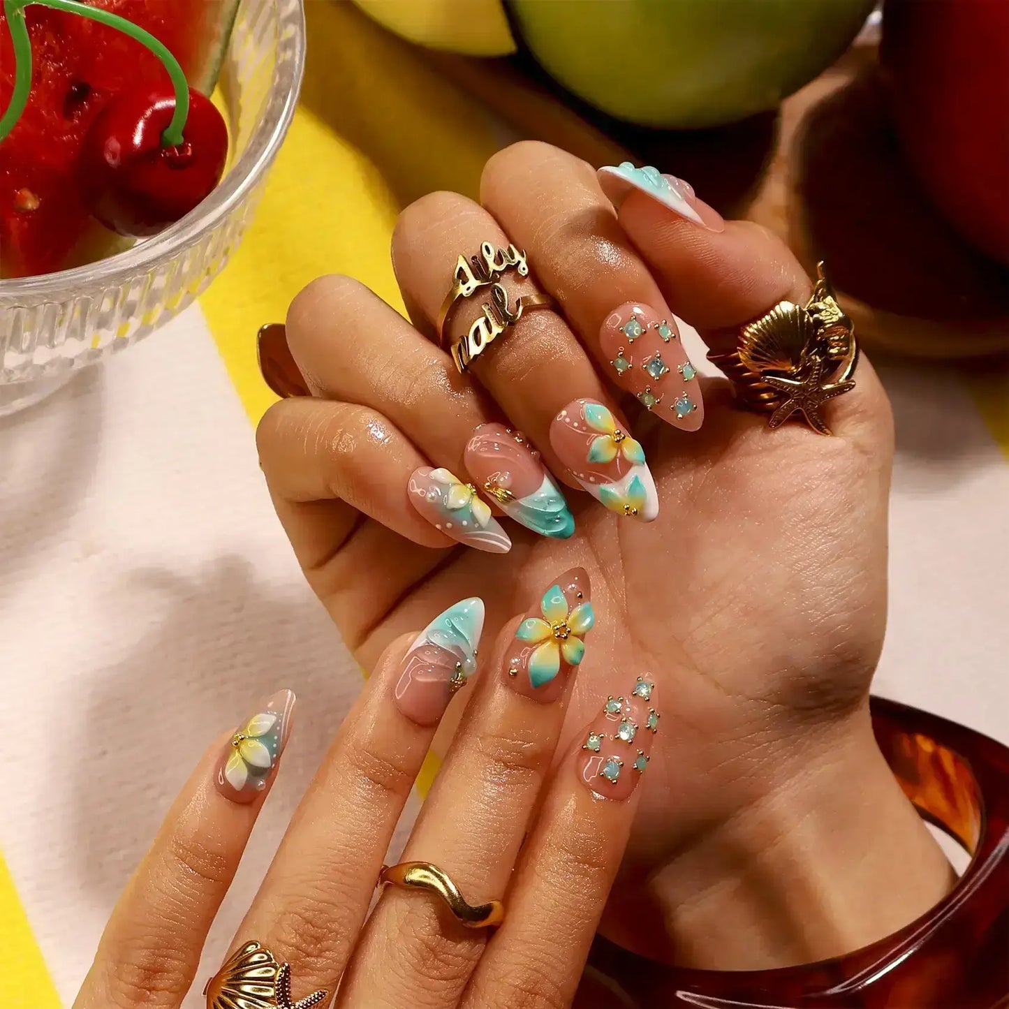 Handmade summer press-on nails with teal aqua tips, hand-painted tropical blooms and gold crystal embellishments by Lily Nails Art