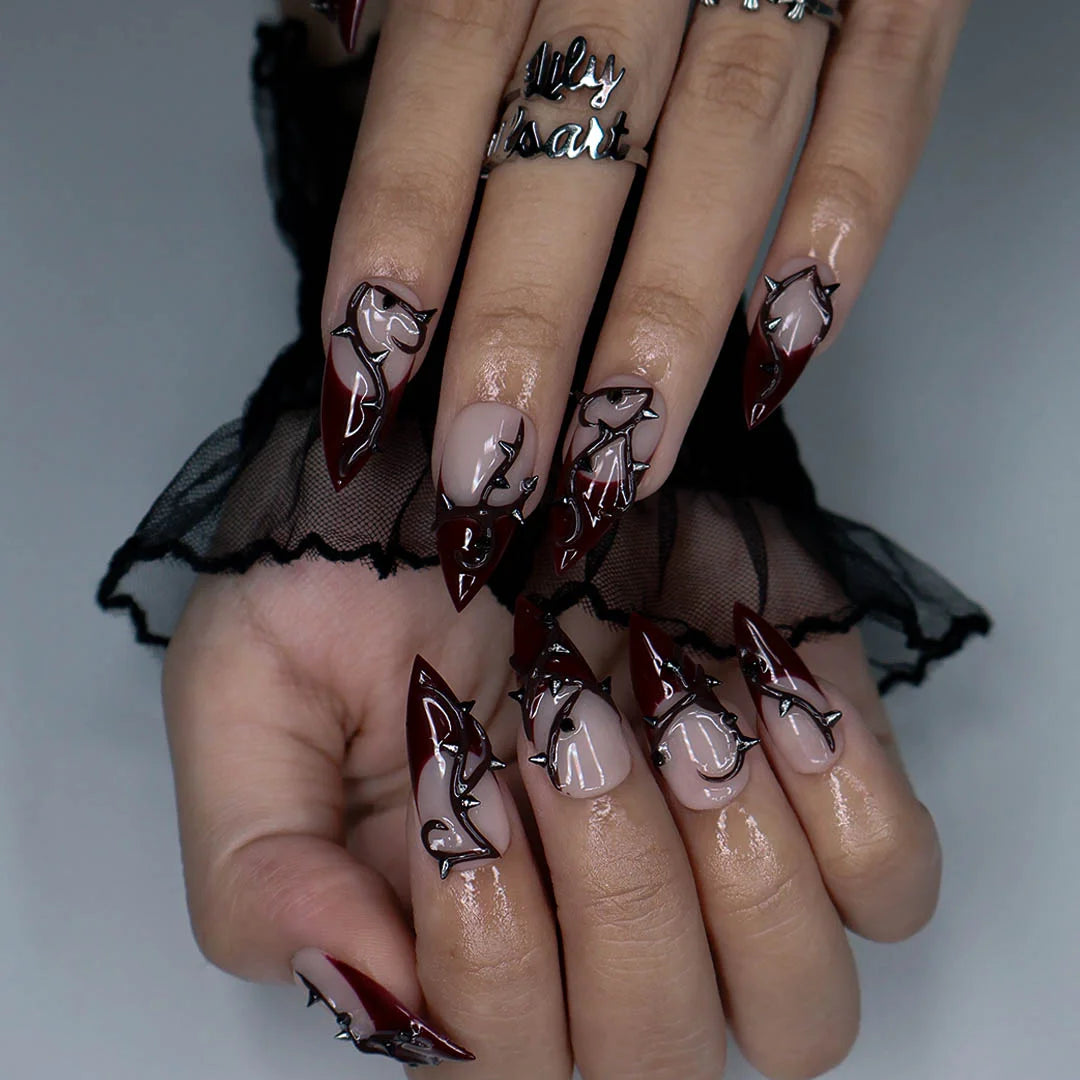 Forbidden gothic press on nails in nude and blood-red French tips with sculpted 3D thorny vines and silver spikes — handmade Halloween press on nails, long stiletto fake nails and gothic nail art.
