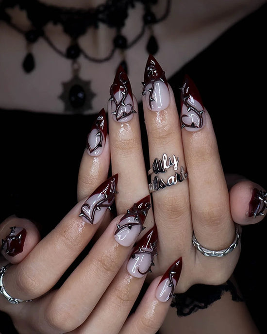 Forbidden gothic press on nails in nude and blood-red French tips with sculpted 3D thorny vines and silver spikes — handmade Halloween press on nails, long stiletto fake nails and gothic nail art.