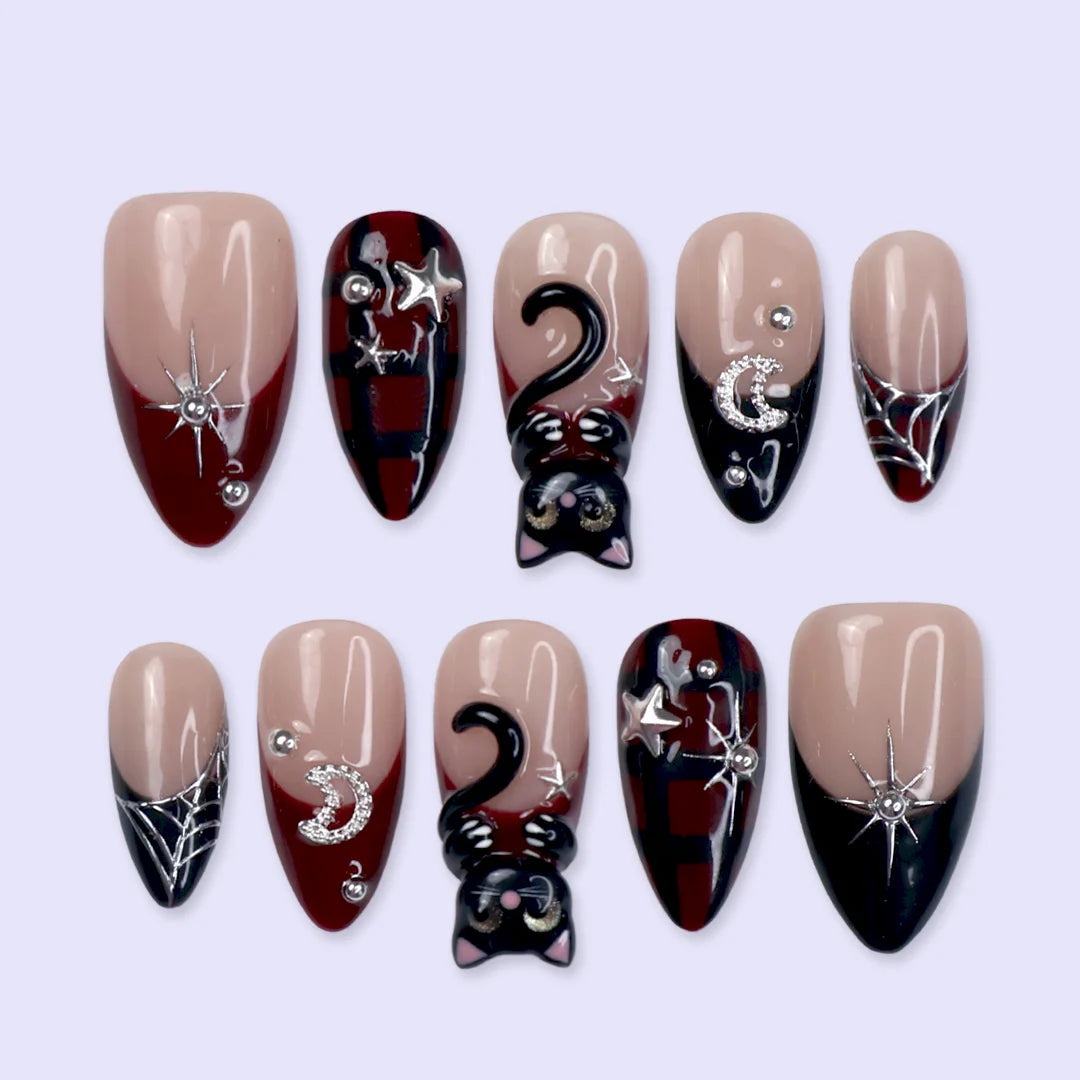 Meow gothic Halloween press on nails in nude, dark red and black with adorable 3D black cats, rhinestone moons, silver stars, spiderwebs and plaid accents — handmade designer press on nails, medium almond fake nails and cute witchy nail art.