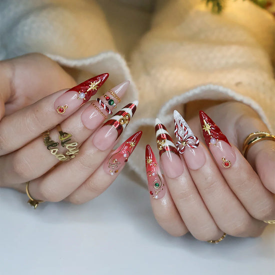 Clausette handmade Christmas press-on nails — long almond set in nude and red with 3D candy-cane bows, gold stripes, starbursts, red and green gemstones and pearl accents.