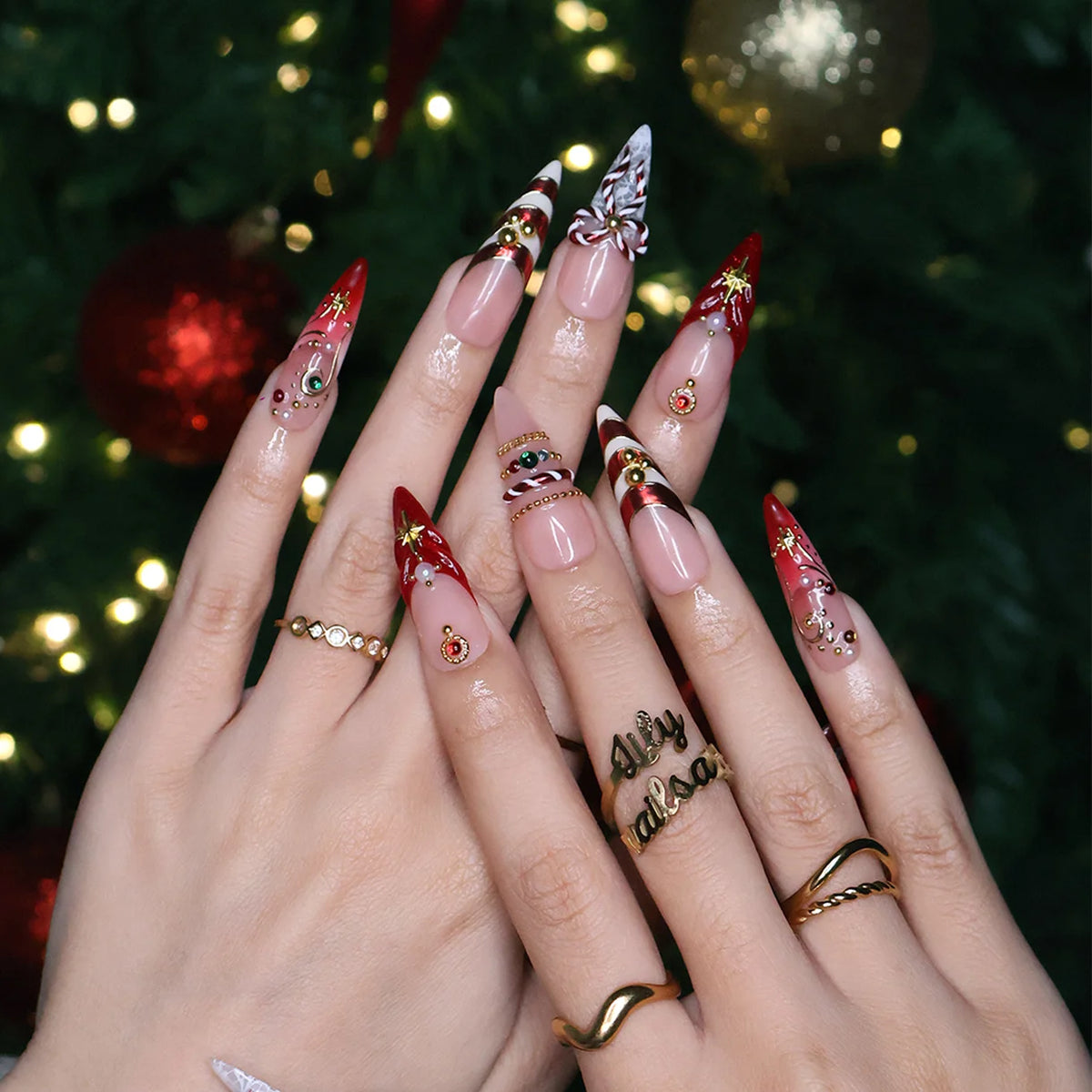 Clausette handmade Christmas press-on nails — long almond set in nude and red with 3D candy-cane bows, gold stripes, starbursts, red and green gemstones and pearl accents.