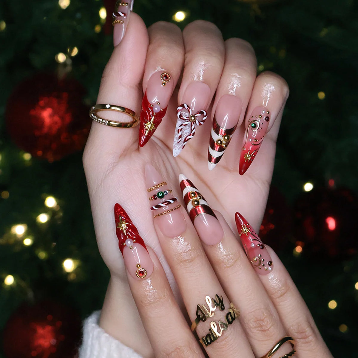 Clausette handmade Christmas press-on nails — long almond set in nude and red with 3D candy-cane bows, gold stripes, starbursts, red and green gemstones and pearl accents.