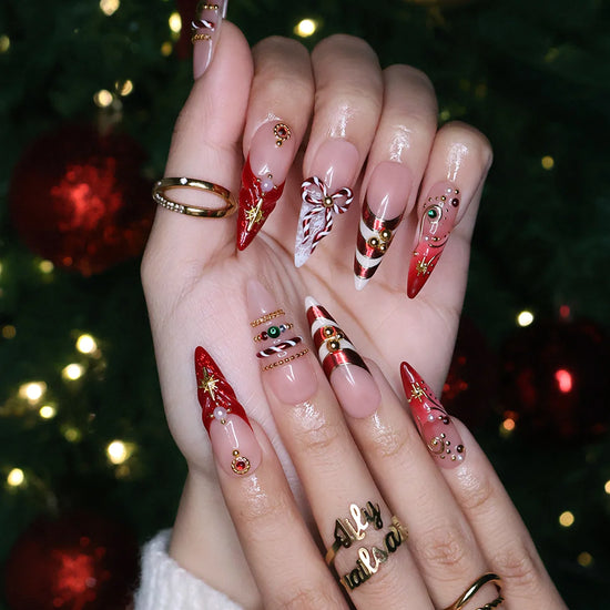 Clausette handmade Christmas press-on nails — long almond set in nude and red with 3D candy-cane bows, gold stripes, starbursts, red and green gemstones and pearl accents.
