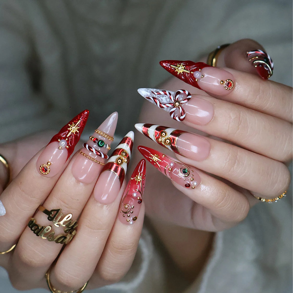 Clausette handmade Christmas press-on nails — long almond set in nude and red with 3D candy-cane bows, gold stripes, starbursts, red and green gemstones and pearl accents.