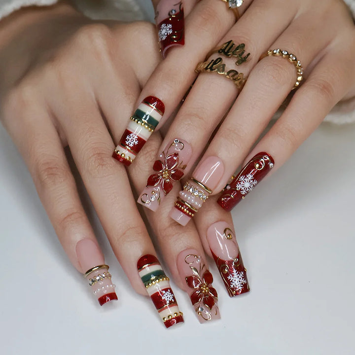 Poinsettia handmade Christmas press-on nails — long square set in nude and red glitter with 3D gold-outlined poinsettia flowers, white snowflakes, gold swirls, festive stripes and pearl accents.