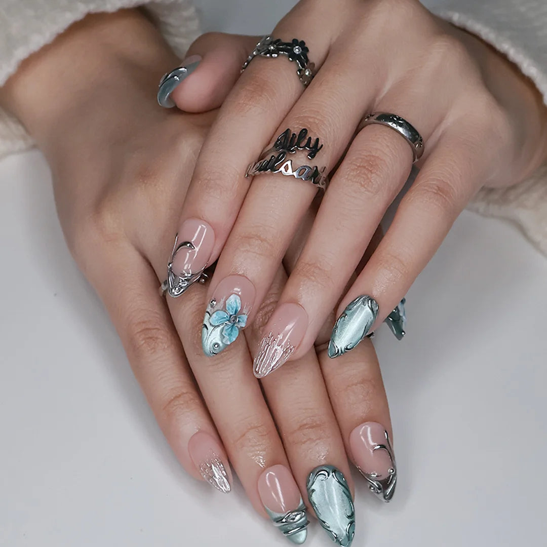 Frostbite handmade Christmas press-on nails — medium almond set in nude with mint and ice-blue cat-eye French tips, silver liquid-metal swirls, 3D baby-blue flowers and sparkling crystal accents.