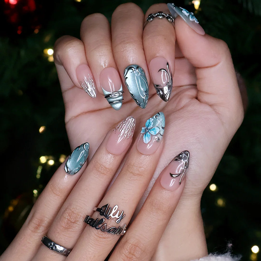 Frostbite handmade Christmas press-on nails — medium almond set in nude with mint and ice-blue cat-eye French tips, silver liquid-metal swirls, 3D baby-blue flowers and sparkling crystal accents.