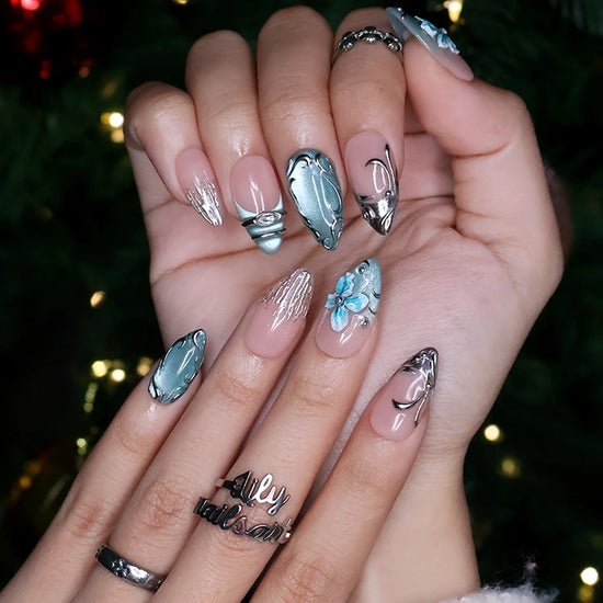 Frostbite handmade Christmas press-on nails — medium almond set in nude with mint and ice-blue cat-eye French tips, silver liquid-metal swirls, 3D baby-blue flowers and sparkling crystal accents.