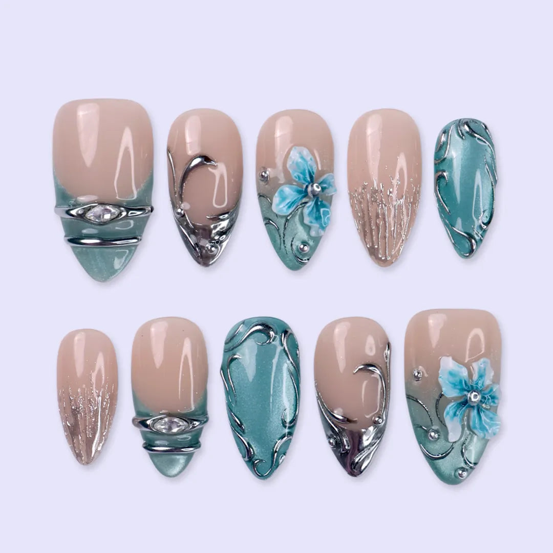 Frostbite handmade Christmas press-on nails — medium almond set in nude with mint and ice-blue cat-eye French tips, silver liquid-metal swirls, 3D baby-blue flowers and sparkling crystal accents.