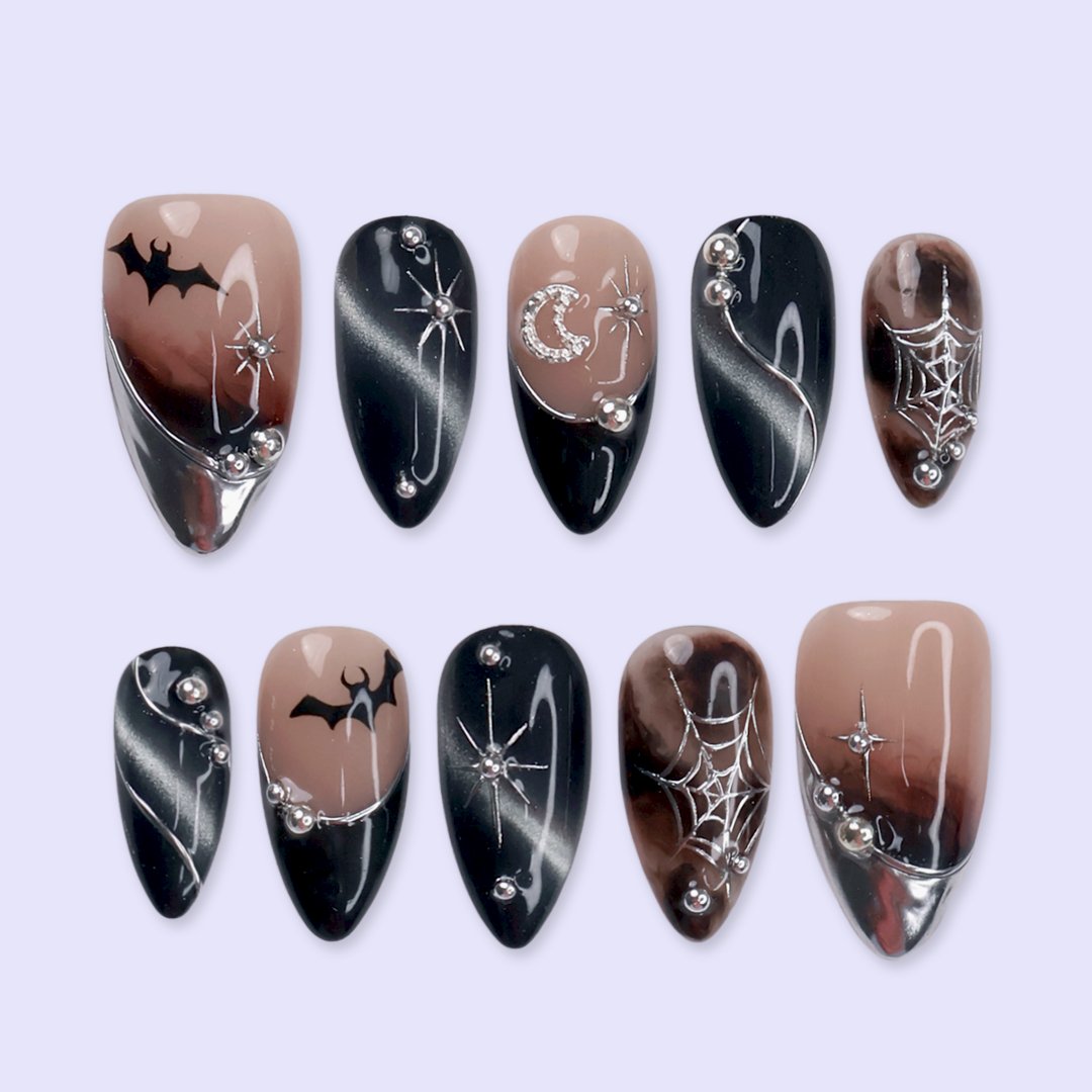 Batwing handmade gothic Halloween press-on nails — medium almond set in nude, black cat-eye and smoky brown with silver chrome tips, bats, rhinestone crescent moon and silver spiderwebs.