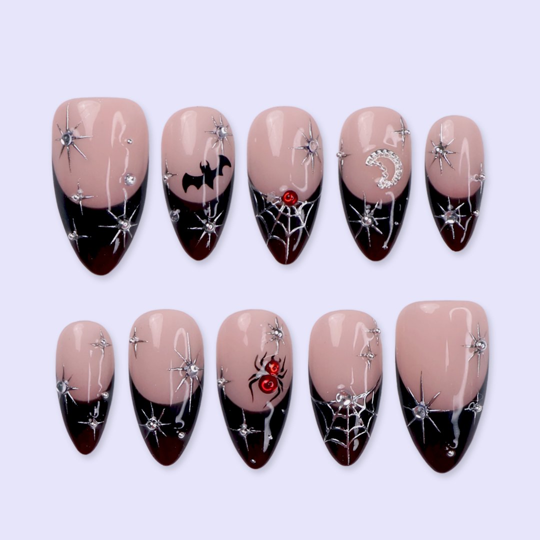 Samhain handmade gothic Halloween press-on nails — medium almond set in nude with black French tips, silver starbursts, bat, jeweled spider, spiderwebs and crescent moon.