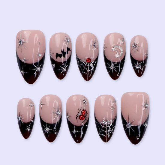 Samhain handmade gothic Halloween press-on nails — medium almond set in nude with black French tips, silver starbursts, bat, jeweled spider, spiderwebs and crescent moon.