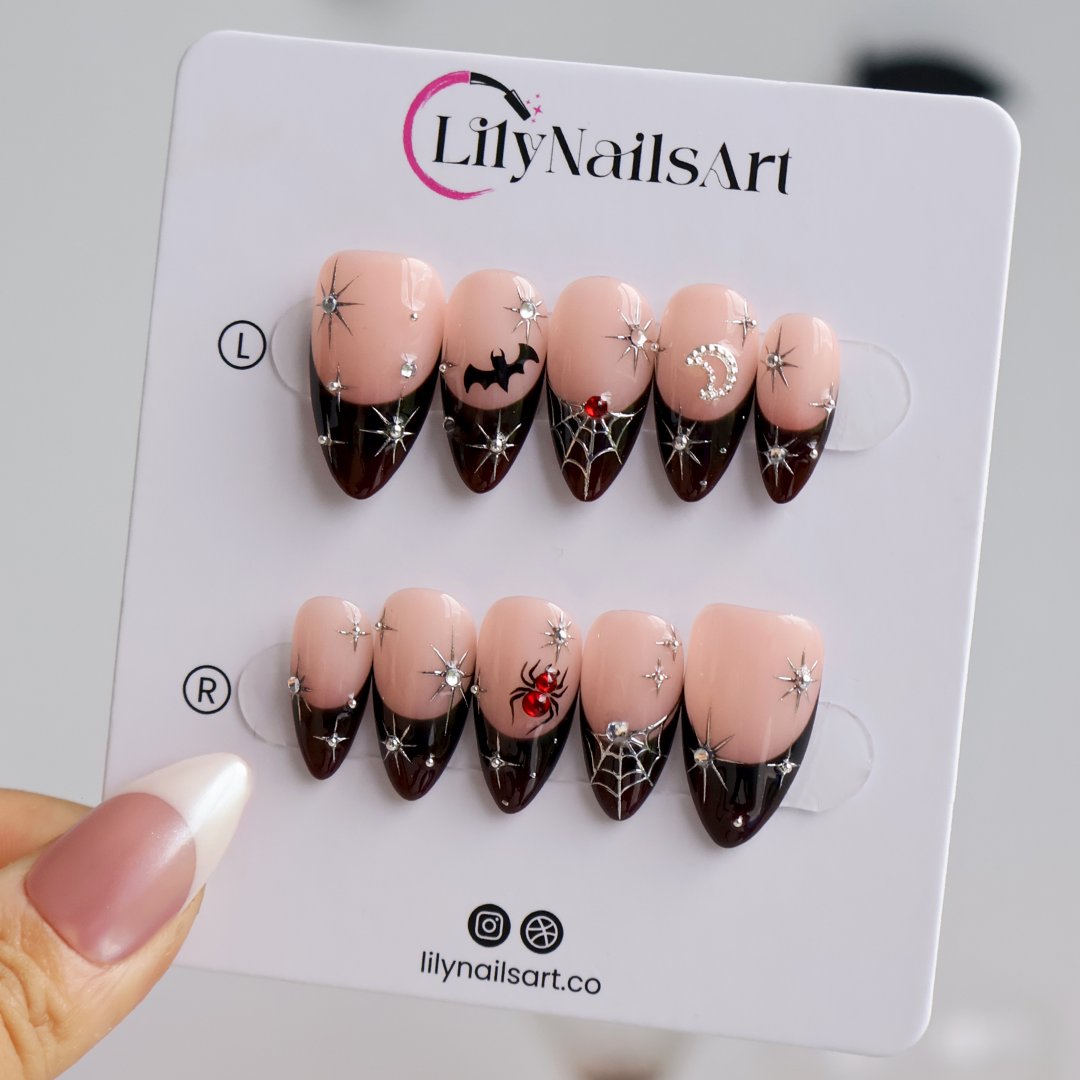 Samhain handmade gothic Halloween press-on nails — medium almond set in nude with black French tips, silver starbursts, bat, jeweled spider, spiderwebs and crescent moon.