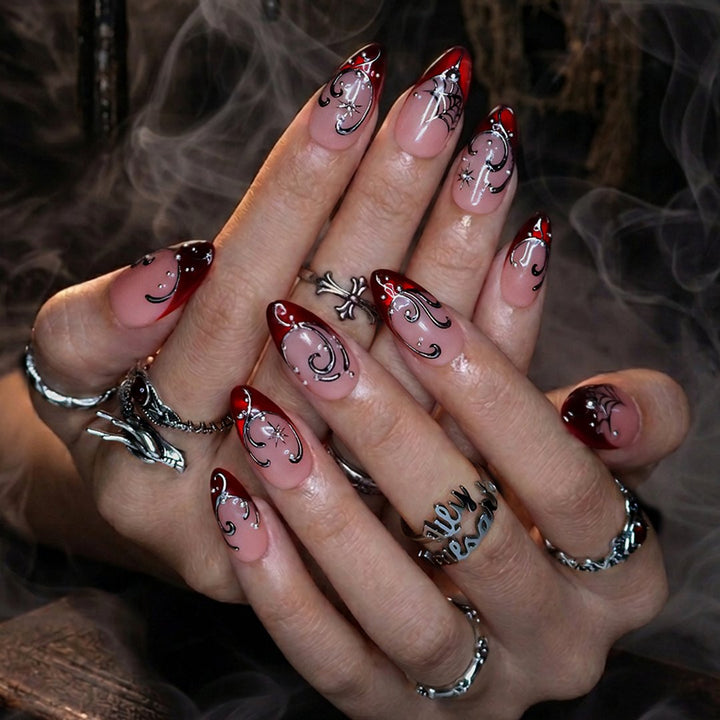 Siren handmade gothic press-on nails — medium almond set in glossy nude with blood-red French tips, silver swirls, spiderwebs, crystal accents and celestial starbursts.