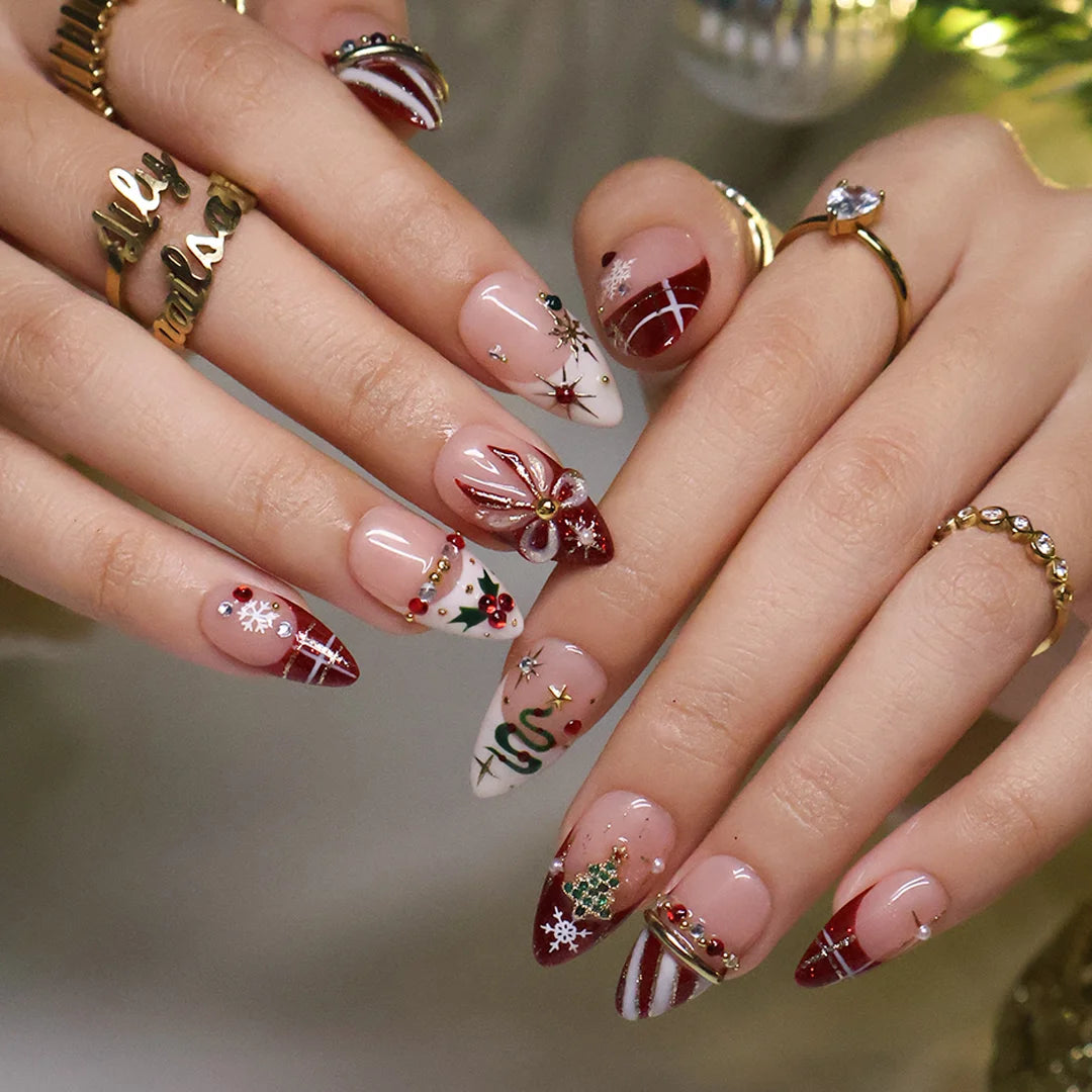 Jubilee handmade Christmas press-on nails — medium almond set in nude, red and cream with a glitter Christmas tree, snowflakes, red plaid, gold bow, holly berries, candy-cane stripes and gold star accents.