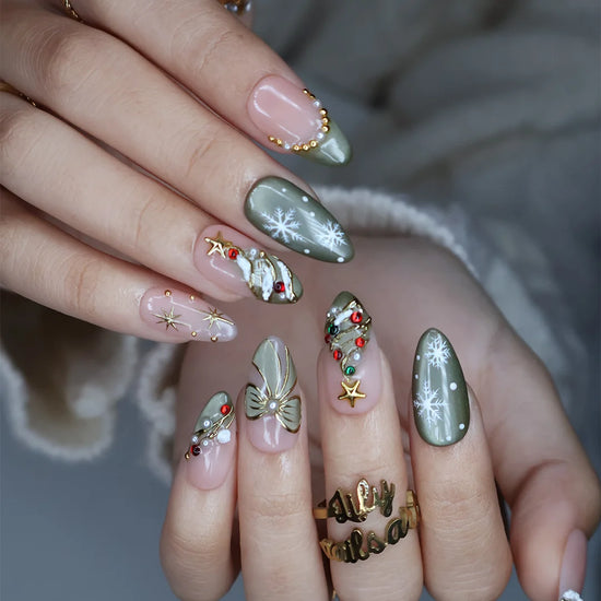 Wintergreen handmade Christmas press-on nails — medium almond set in nude and sage-green cat-eye with a 3D gold-star Christmas tree, delicate snowflakes, gold bow, ornament baubles and red-green gemstone accents.