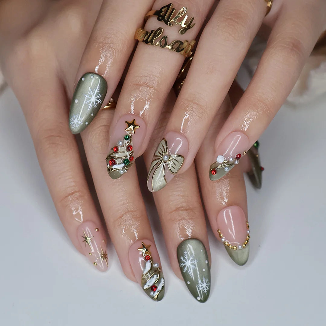 Wintergreen handmade Christmas press-on nails — medium almond set in nude and sage-green cat-eye with a 3D gold-star Christmas tree, delicate snowflakes, gold bow, ornament baubles and red-green gemstone accents.